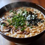 Un bol de ramen végétarien avec un bouillon crémeux, garni de champignons tranchés, d'oignons verts, d'algues et de graines de sésame.